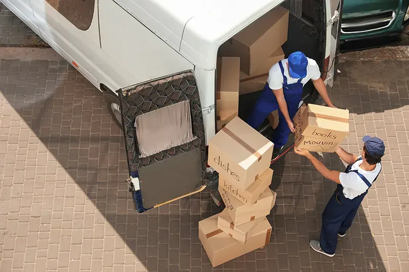 Movers carrying boxes beside an open removal van
