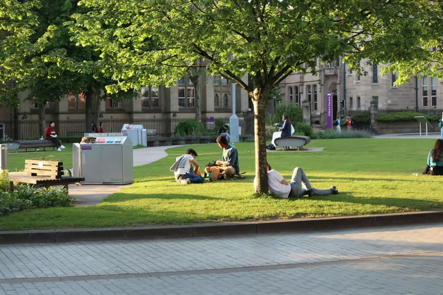 Students relaxing on a sunny university campus lawn in Manchester, enjoying downtime between studies