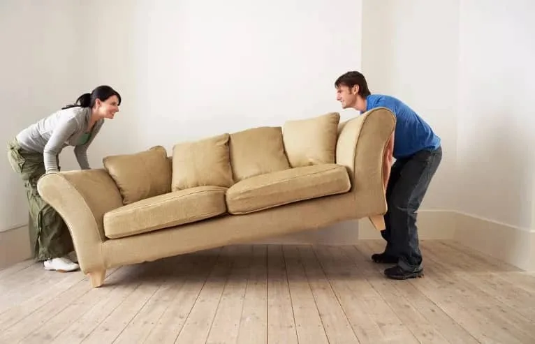 Two people carrying a sofa across a room
